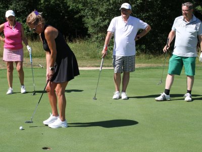 Eine Gruppe von vier Personen spielt Golf auf einem Platz. Eine Person versucht, den Ball ins Loch zu bringen.