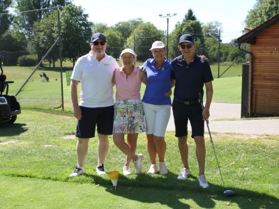 Vier Personen stehen auf einem Golfplatz und genießen das Spiel. Es ist ein sonniger Tag und es gibt viele Bäume.