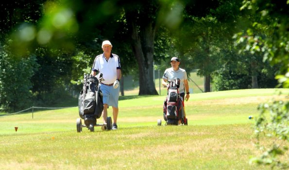 Golfspieler gehen auf dem Golfplatz Zwei Männer gehen mit Golftaschen über das Grün eines Golfplatzes. Es ist tagsüber und sonnig.