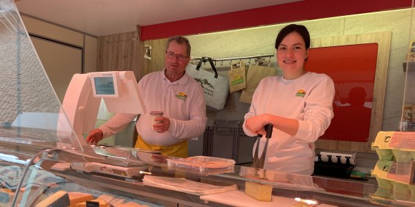 Zwei Verkäufer*innen der Käserei Diepolz stehen auf dem Isnyer Wochenmarkt hinter der Theke ihres Verkaufswagens.