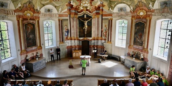 In einer alten Kirche stehen Menschen versammelt und hören gespannt den Worten von Pastoralreferent Benjamin Sigg zu.