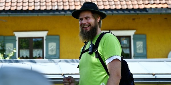 Der Adelegg Ranger mit grünem Shirt lächelt fröhlich während der Pilgerwanderung.