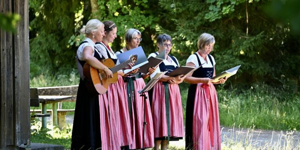 Fünf Frauen in Tracht singen und musizieren draußen in einer schönen Umgebung während eines sonnigen Tages.
