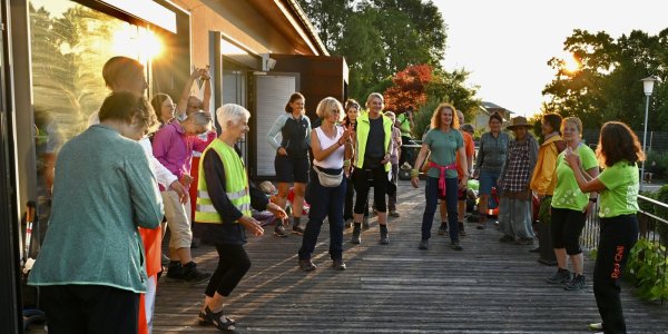 Eine Gruppe von Menschen übt gemeinsam auf der Terrasse während des Sonnenuntergangs, erfreut sich der frischen Luft und der Gemeinschaft.