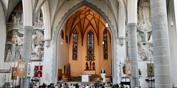 Eine große Gruppe von Menschen nimmt an einem Gottesdienst in einer historischen Kirche teil und hört einem Priester zu.