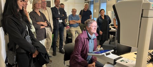 Eine Gruppe von Menschen schaut interessiert auf einen Mann, der an einem Computer arbeitet, im Büroin Isny.