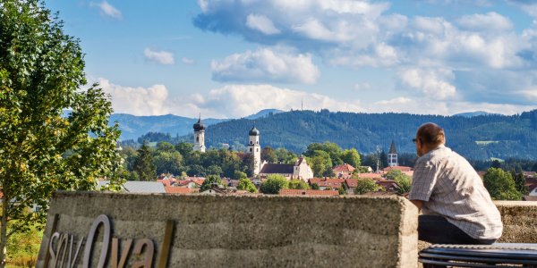 Ein Mann genießt die Aussicht auf die Türme und Tore der Isnyer Altstadt vom Aussichtspunkt Isny Oval.