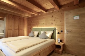 Helles Zimmer mit Doppelbett, viel Holz und grüner Polsterrückwand.