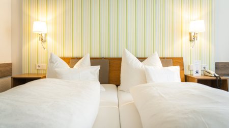 Zwei Betten in einem Hotelzimmer mit einfachem Design Das Zimmer zeigt zwei Einzelbetten mit weißen Bettdecken und Kissen. Es gibt Lampen und eine einfache Wandgestaltung.