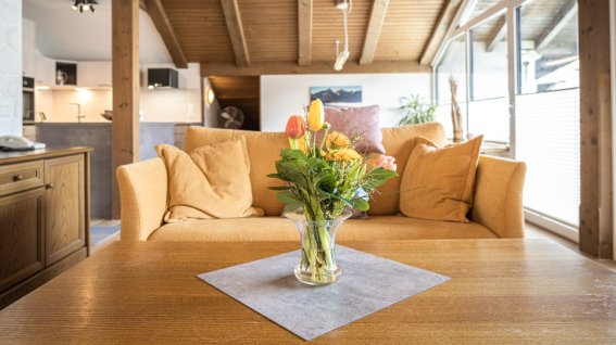Blumen auf dem Tisch in einem Wohnzimmer Eine Vase mit bunten Blumen steht auf einem Tisch in einem Wohnzimmer. Im Hintergrund sieht man das Sofa und die Küche.