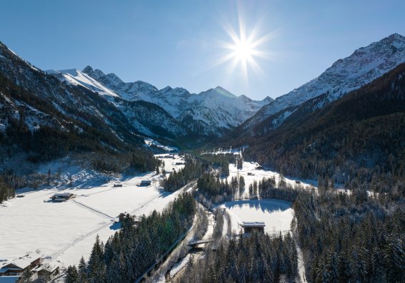 Luftaufnahme des verschneiten Stillachtals bei Oberstdorf im Winter mit strahlender Sonne, verschneiten Wäldern und den Gipfeln der Allgäuer Alpen.