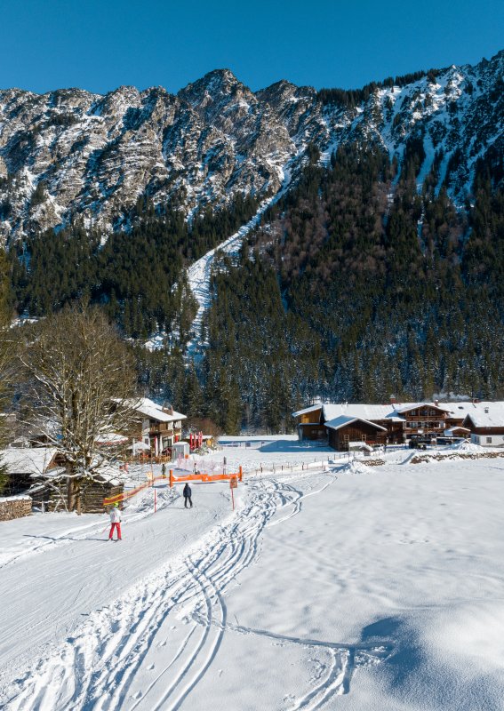 Tief verschneite Wiesen mit Spuren im Schnee vor dem Landhaus am Fellhorn in Oberstdorf, dahinter verschneite Berghänge unter blauem Winterhimmel.