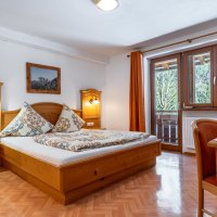 Das Zimmer hat ein großes Bett und einen Tisch. Große Fenster zeigen den Blick auf die Alpen. Es ist hell und gemütlich.