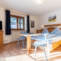 Der Raum zeigt ein Bett, einen Tisch und einen Fernseher in einer gemütlichen Umgebung in einer Unterkunft am Tag.