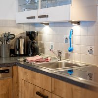 Die Küche zeigt eine Arbeitsfläche mit Geräten und Utensilien. Ein Wasserhahn und eine Spüle sind sichtbar.