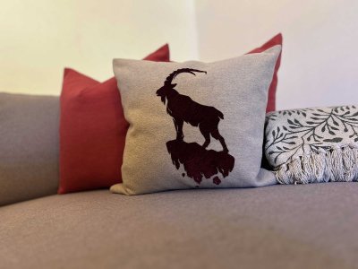 Ein Kissen mit dem Bild eines Steinbocks liegt auf der Couch. Die Couch hat verschiedene Kissen in anderen Farben.