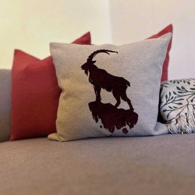 Ein Kissen mit dem Bild eines Steinbocks liegt auf der Couch. Die Couch hat verschiedene Kissen in anderen Farben.