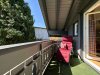 Ein Balkon mit einem roten Stuhl und grünen Pflanzen an einem sonnigen Tag. Die Sonne scheint und es ist windstill.