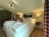 Das Schlafzimmer zeigt ein Bett mit Kissen und einfachen Möbeln. Es gibt einen Teppich und Bilder an der Wand.