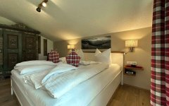 Das Schlafzimmer zeigt ein Bett mit Kissen und einfachen Möbeln. Es gibt einen Teppich und Bilder an der Wand.