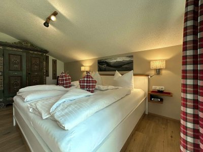 Das Schlafzimmer zeigt ein Bett mit Kissen und einfachen Möbeln. Es gibt einen Teppich und Bilder an der Wand.