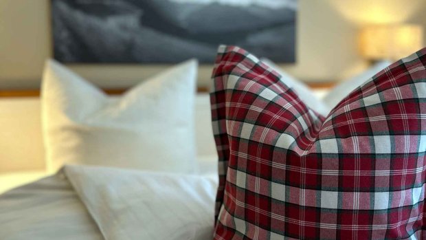 Dekoratives Design Ferienwohnung Kuhgehren Es gibt ein Bett mit einem karierten Kissen und einem weiteren weißen Kissen im Hintergrund.