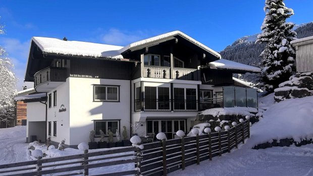 Haus im Schnee vor blauem Himmel Es liegt Schnee um das Haus in den Bergen. Der Himmel ist blau und die Sonne scheint. Familien besuchen die Gegend.