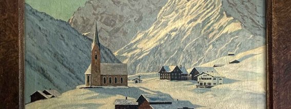 Das Bild zeigt ein Bergdorf im Winter. Am Hintergrund sind hohe Berge und eine Kirche zu sehen.
