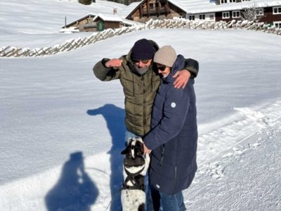 Ein Mann und eine Frau stehen im Schnee. Sie haben einen Hund dabei. Es ist ein sonniger Tag in den Bergen.