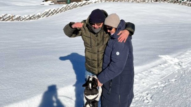Ein Paar steht im Schnee mit einem Hund Ein Mann und eine Frau stehen im Schnee. Sie haben einen Hund dabei. Es ist ein sonniger Tag in den Bergen.