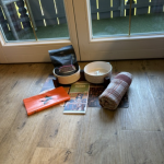Unser Hundepaket aus Handtuch, Hundetüten, Karte, Fressnapf und Leckerli Auf dem Boden liegen verschiedene Gegenstände wie Schalen, ein Handtuch, eine Decke und ein Buch.