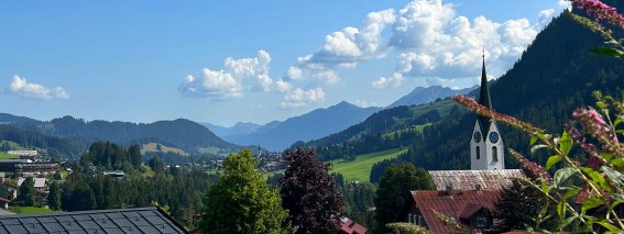 Wolken ziehen über die Berge in Deutschland. Eine Kirche steht im Vordergrund mit Bäumen und Häusern.