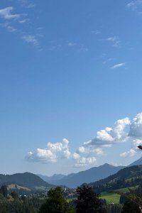 Die Berge sind zu sehen, und der Himmel ist blau mit Wolken. Es ist Nachmittag und in der Ferne gibt es Wald und Felder.