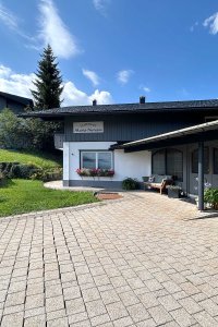 Ein Haus mit einem Garten und gepflasterter Einfahrt. Es steht in einer ruhigen Wohngegend. Wolken sind am Himmel.