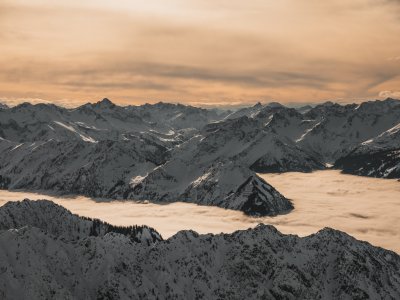 Der wunderschöne Sonnenuntergang taucht die verschneiten Alpen in warmes Licht, während Wolken wie ein Meer unter den Gipfeln liegen.