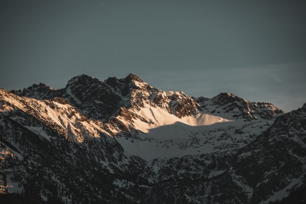 Die Sonne beleuchtet die schneebedeckten Gipfel der Berge in der Abenddämmerung. Ein malerisches Naturpanorama entsteht.