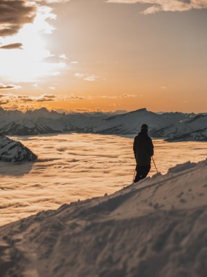 Ein Skifahrer genießt den Blick auf die schneebedeckten Berge und Wolken bei Sonnenuntergang