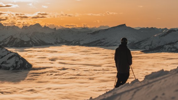 Ein Skifahrer genießt den Blick auf die schneebedeckten Berge und Wolken bei Sonnenuntergang