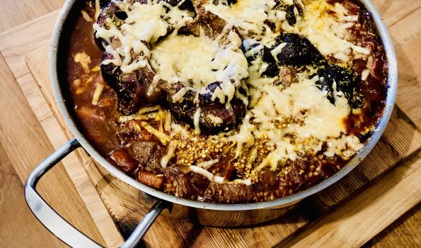 Gericht mit Käse und Saucen in einer Pfanne Dieses Gericht zeigt eine Pfanne mit Käse und verschiedenen Soßen. Es steht auf einem Holzbrett und sieht lecker aus.