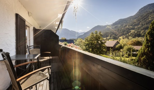 Ein Balkon mit Stühlen bietet eine Aussicht auf die Berge am Nachmittag. Die Sonne scheint und die Natur ist sichtbar.