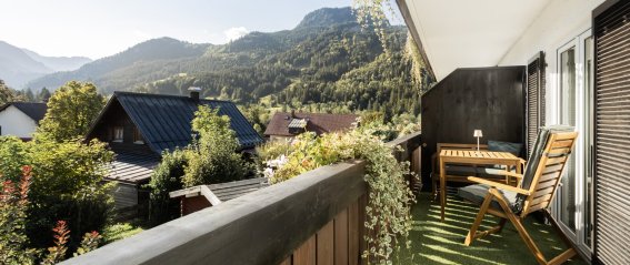 Ein Balkon zeigt einen schönen Blick auf Berge und Gärten. Der Himmel ist blau und die Pflanzen sind grün.