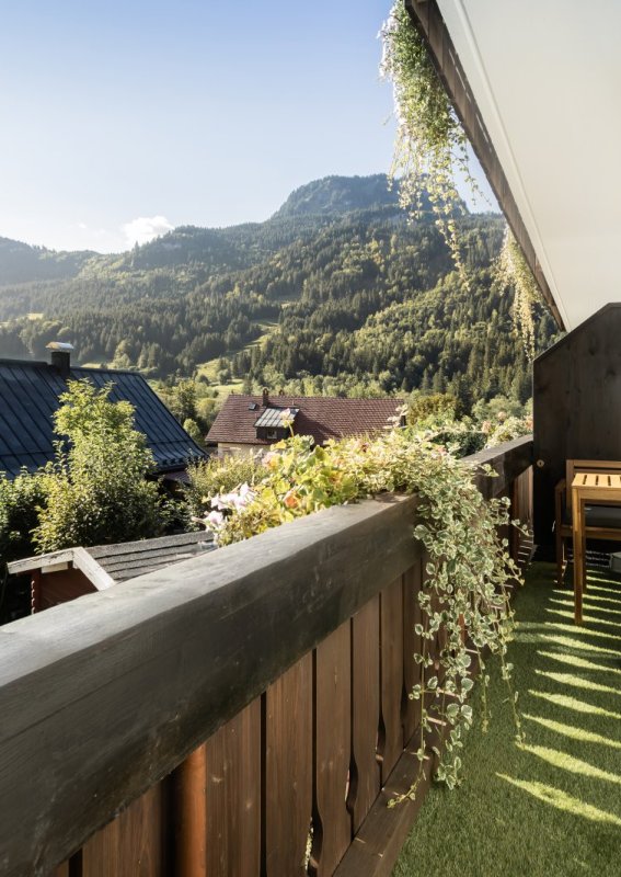 Ein Balkon zeigt einen schönen Blick auf Berge und Gärten. Der Himmel ist blau und die Pflanzen sind grün.