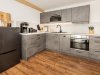 Moderne Küche mit Elektrogeräten und Holzfußboden In einer modernen Küche sind Elektrogeräte wie ein Kühlschrank und eine Kaffeemaschine sichtbar. Der Boden ist aus Holz.