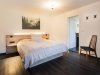 Schlafzimmer mit Bett und einfachem Design In einem hellen Raum steht ein Bett mit weißer Bettwäsche. Ein Stuhl und ein Bild hängen an der Wand.