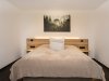 Schlafzimmer mit einem Bett und einem Gemälde In einem einfachen Schlafzimmer steht ein Bett vor einem Gemälde an der Wand. Die Wände sind weiß und der Boden ist dunkel.