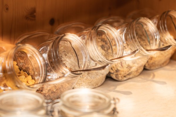 Es gibt mehrere Gläser mit Cerealien auf einem Tisch. Jedes Glas hat einen Löffel. Die Gläser sind beschriftet.