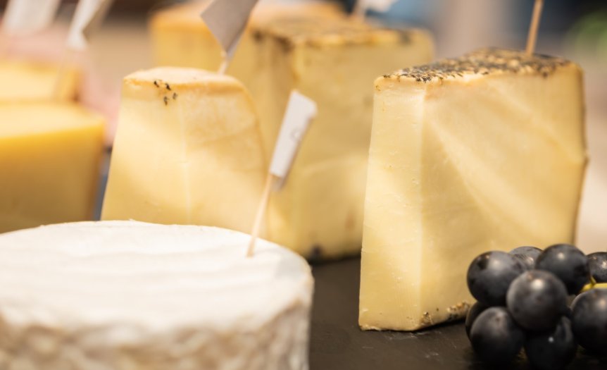 Auf einem Tisch stehen verschiedene Käsesorten und Trauben. Es gibt kleine Fähnchen zur Kennzeichnung der Käse.
