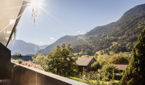 Die Sonne scheint auf die Berge und Bäume in der Ferne. Die Landschaft ist grün mit Hütten und einer ruhigen Atmosphäre.