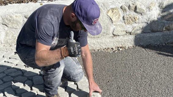 Ein Handwerker verlegt Steine und bereitet die Pflasterung auf einer Baustelle im Freien vor.