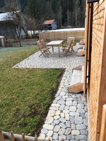 Neugestaltete Terrasse aus Steinen mit Sitzgelegenheiten in einem ruhigen, ländlichen Gebiet im Frühling.